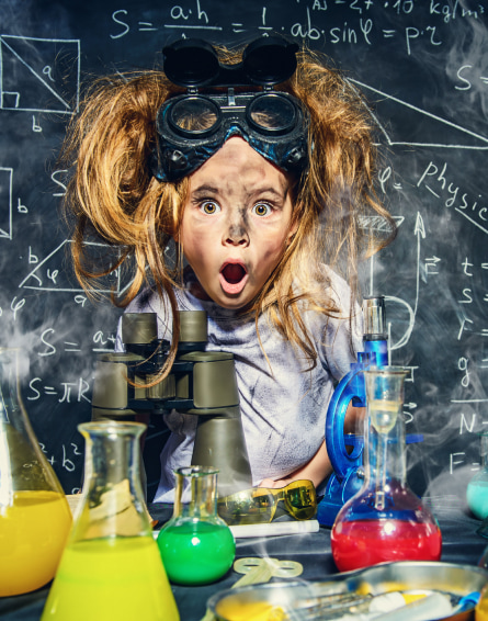 Excited child with oversized goggles and hair standing on end in a makeshift lab.