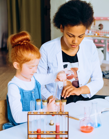A girl with red hair assisted by her teacher in conducting a science experiment with test tubes on a table.