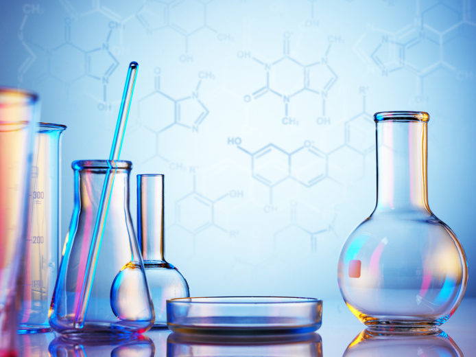 Empty laboratory glassware on a reflective surface with a backdrop of chemical formulas.